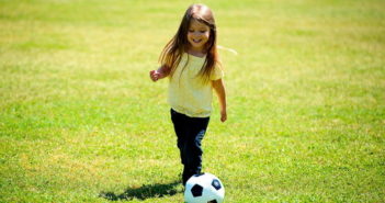 Girl kicking soccer ball on the grass
